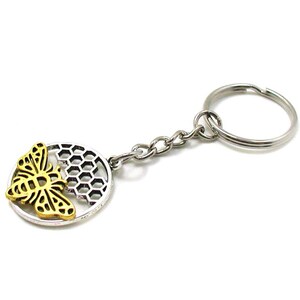 May include: A silver key chain with a round charm featuring a gold bee and honeycomb design.