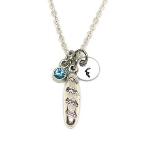 May include: Silver necklace with a baguette charm, a small blue gemstone, and a silver charm with the letter 'F' on it.