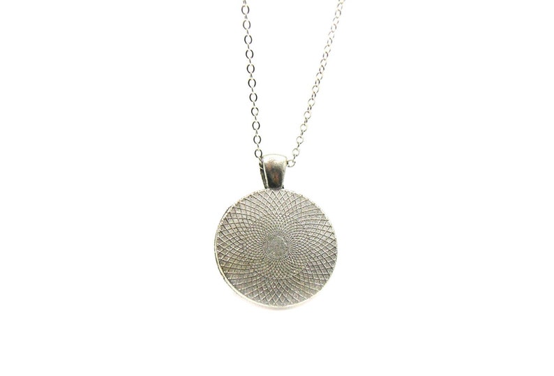 May include: Silver necklace with a round pendant featuring a detailed, circular design.