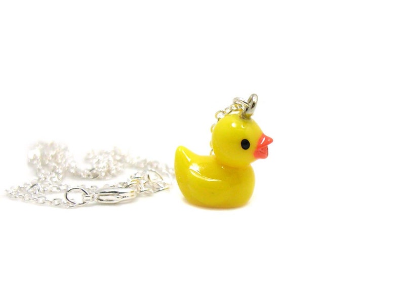 May include: A yellow rubber ducky charm necklace with a silver chain. The ducky has a red beak and black eyes.