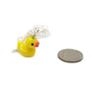 May include: A yellow rubber ducky charm on a silver chain necklace. The ducky charm has a red beak and a small silver loop on top. The necklace is about 18 inches long.