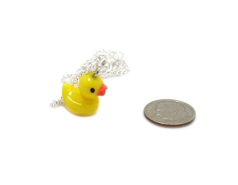 May include: A yellow rubber ducky charm on a silver chain necklace. The ducky charm has a red beak and a small silver loop on top. The necklace is about 18 inches long.