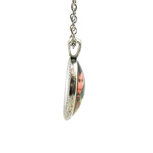 May include: A silver chain necklace with a round pendant featuring a colorful image of a person with a red and black design.