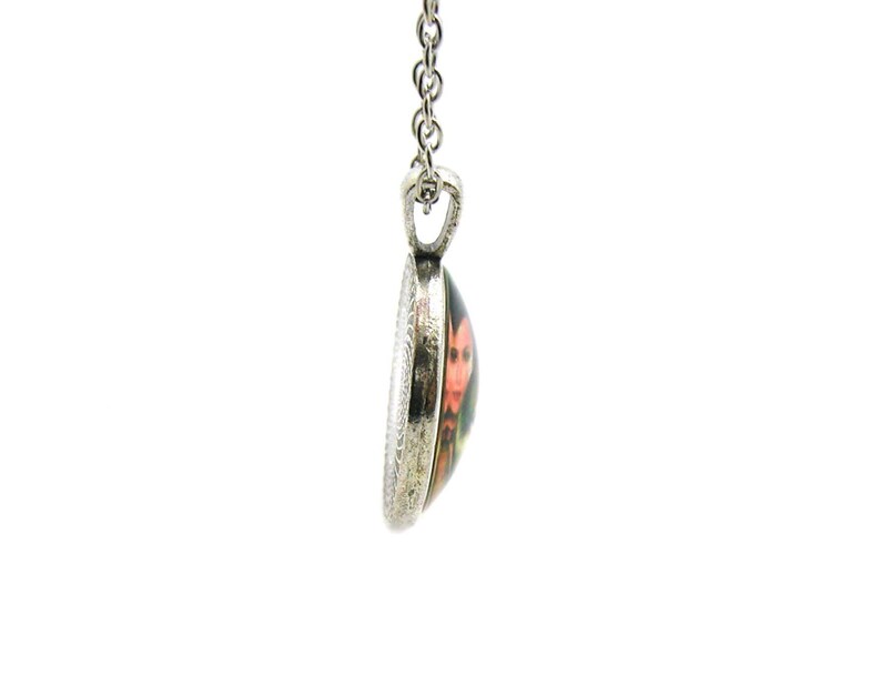 May include: A silver chain necklace with a round pendant featuring a colorful image of a person with a red and black design.