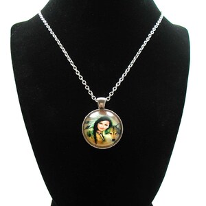 May include: A silver chain necklace with a round glass pendant featuring a woman with a wolf. The pendant has a silver border and the image is of a woman with long dark hair and a wolf with brown fur.