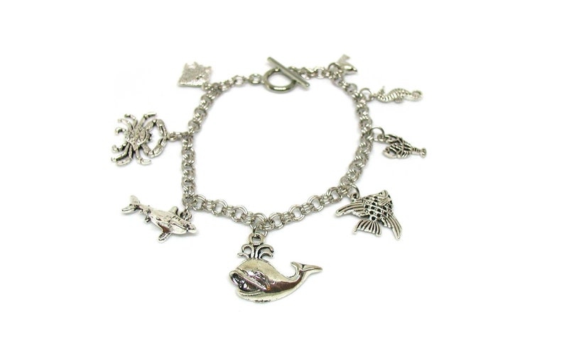 May include: Silver charm bracelet with a variety of sea creature charms, including a whale, dolphin, crab, seahorse, and fish.