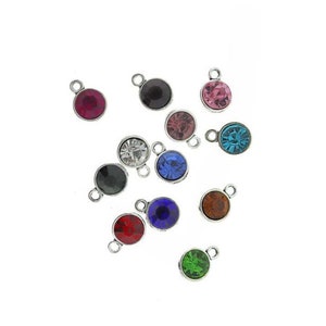 Puede incluir: Surtido de 12 colgantes de plata con brillantes de colores. Cada colgante presenta un brillante redondo y facetado de un color diferente, incluyendo rojo, rosa, azul, verde, negro y transparente.