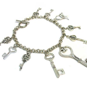 May include: A silver charm bracelet with multiple key-shaped charms. The bracelet has a silver clasp and is made of a chain link design.