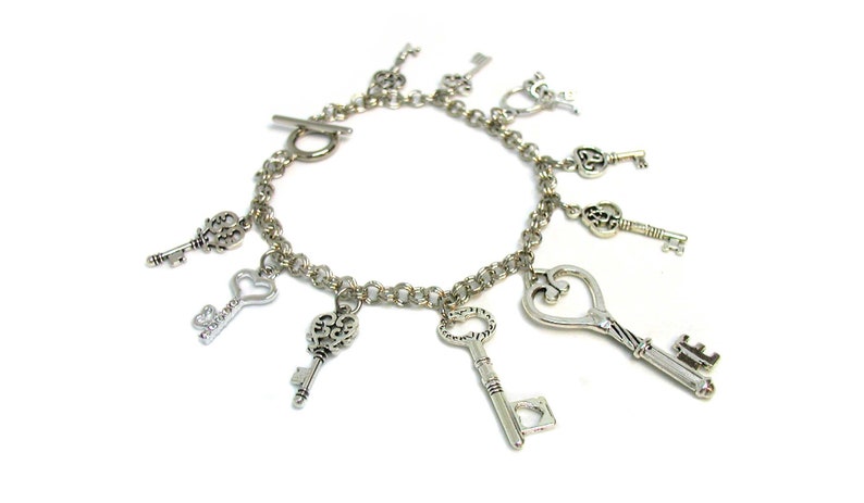 May include: A silver charm bracelet with multiple key-shaped charms. The bracelet has a silver clasp and is made of a chain link design.