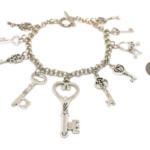 May include: A silver charm bracelet with multiple key charms. The bracelet is made of a silver chain and has a lobster clasp closure. The charms are all different shapes and sizes, and some have intricate designs.