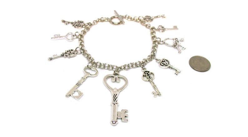 May include: A silver charm bracelet with multiple key charms. The bracelet is made of a silver chain and has a lobster clasp closure. The charms are all different shapes and sizes, and some have intricate designs.