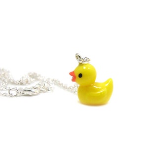 May include: A yellow rubber ducky charm necklace with a silver chain. The ducky has black eyes and a red beak.