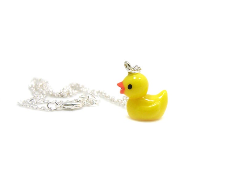 May include: A yellow rubber ducky charm necklace with a silver chain. The ducky has black eyes and a red beak.