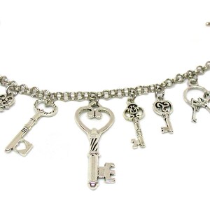 May include: A silver charm bracelet with multiple key charms. The bracelet has a lobster clasp closure and a t-bar closure. The keys are all different shapes and sizes, and some have intricate designs.