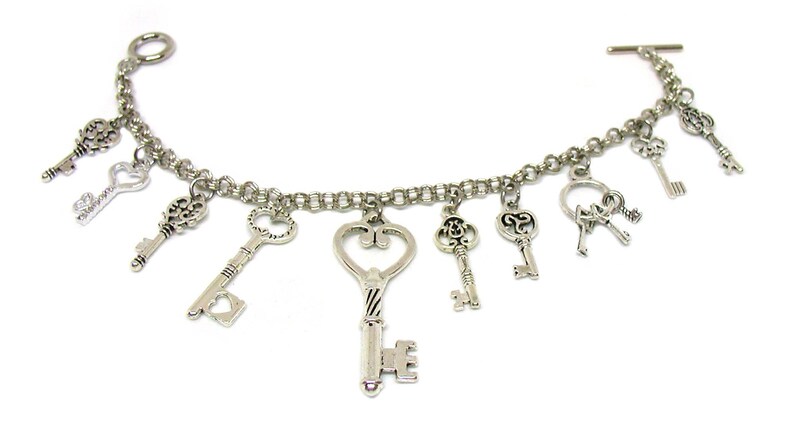 May include: A silver charm bracelet with multiple key charms. The bracelet has a lobster clasp closure and a t-bar closure. The keys are all different shapes and sizes, and some have intricate designs.