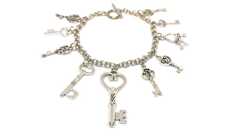 May include: A silver charm bracelet with multiple key charms. The bracelet has a silver chain and a lobster clasp closure. The key charms are all different shapes and sizes, and some have intricate details.
