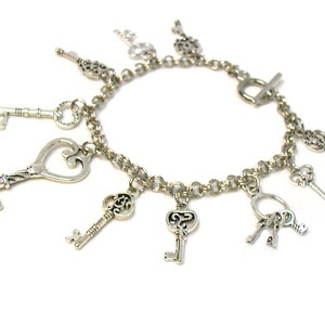 May include: A silver charm bracelet with multiple key charms. The bracelet has a silver chain and a toggle clasp. The charms are all different shapes and sizes, and some have intricate designs.