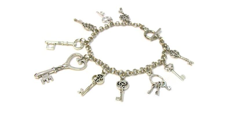 May include: A silver charm bracelet with multiple key charms. The bracelet has a silver chain and a toggle clasp. The charms are all different shapes and sizes, and some have intricate designs.