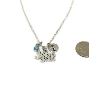 Puede incluir: Collar de plata con un dije que dice "John 3:16" y un peque&ntilde;o cristal azul. Tambi&eacute;n hay un peque&ntilde;o dije de plata con la letra "E" en &eacute;l. El collar se muestra junto a una moneda de euro para comparar el tama&ntilde;o.
