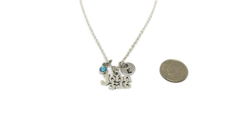Puede incluir: Collar de plata con un dije que dice "John 3:16" y un peque&ntilde;o cristal azul. Tambi&eacute;n hay un peque&ntilde;o dije de plata con la letra "E" en &eacute;l. El collar se muestra junto a una moneda de euro para comparar el tama&ntilde;o.