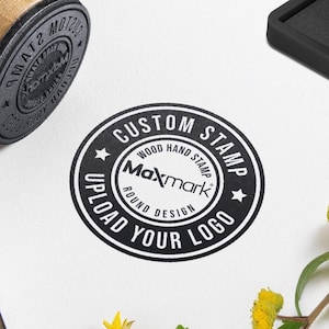 May include: A black and white round custom stamp with the text "CUSTOM STAMP" and "UPLOAD YOUR LOGO" around the edge. The text "WOOD HAND STAMP" and "ROUND DESIGN" are inside the circle. The text "Maxmark" is in the center of the circle.