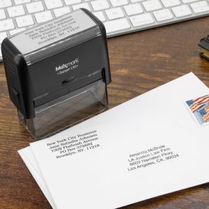 Może przedstawiać: Czarny stempel Maxmark Stamper C40 z tekstem "New York City Business" i informacjami adresowymi. Stempel znajduje się nad białą kopertą z adresem i znaczkiem pocztowym.