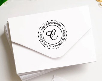 Puede incluir: Una pila de sobres blancos con un sello de dirección personalizado. El sello negro presenta un diseño circular con los nombres "Angel & Peter Collins", dirección y una letra "C" estilizada.