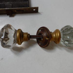 May include: A pair of antique glass door knobs with brass accents. The knobs are faceted and have a clear glass finish.