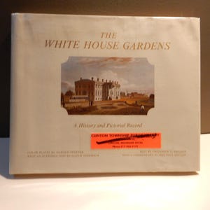 May include: A book titled "The White House Gardens" with a pictorial record of the gardens. The cover features an illustration of the White House and surrounding grounds. The book has a light beige cover with text in a serif font.