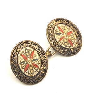 Könnte beinhalten: Vintage Manschettenknöpfe mit ovaler Form und goldfarbenem Finish. Jeder Manschettenknopf hat ein zentrales Blumendesign in Rot, Gelb und Blau auf weißem Hintergrund, umgeben von einem verzierten Rand.