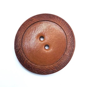 May include: A brown leather button with two holes and a decorative stitched border.