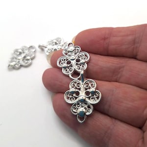 Può includere: Chiusura a bottone in filigrana argentata con un motivo floreale decorativo. La chiusura è composta da due pezzi che si uniscono.