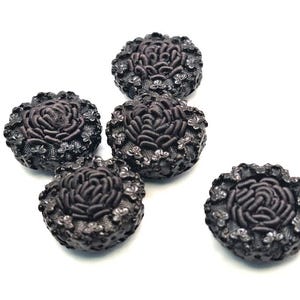 Könnte beinhalten: Fünf schwarze Knöpfe mit einem erhabenen Blumendesign. Die Knöpfe sind rund und haben eine leicht strukturierte Oberfläche.