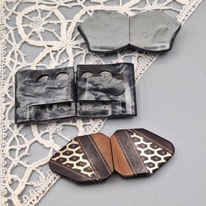 Könnte beinhalten: Drei Sets aus zweiteiligen Verschlüssen. Das obere Set ist glatt grau, das mittlere Set ist schwarz mit marmorierter Textur und kreisförmigen Ausschnitten, und das untere Set ist braun mit einem dunklen geometrischen Muster und goldfarbenen Akzenten.