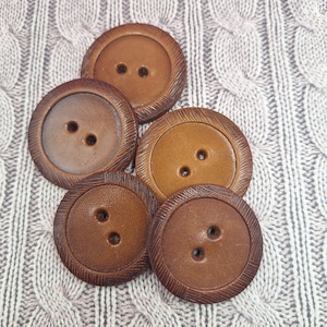 Peut inclure: Un ensemble de cinq gros boutons ronds bruns, avec deux ou trois trous chacun. Les boutons ont un bord texturé et strié, avec des nuances de brun allant du beige clair au chocolat foncé.