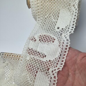 May include: Cream-coloured lace trim on a wooden spool. The lace has a delicate openwork design with scalloped edges. The trim is likely used for sewing, crafting, or adding a decorative touch to garments or home decor projects.