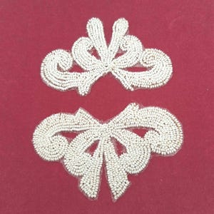 May include: Two white beaded appliqués featuring intricate scrollwork and symmetrical patterns. Each piece is crafted with small, uniform white beads arranged in swirling, decorative shapes that form a cohesive, ornate design for garment embellishment.