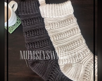 May include: Two crocheted Christmas stockings, one brown and one white, hanging on a wooden surface. The stockings are made with a textured stitch pattern.