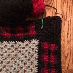 May include: A crocheted blanket with squares in black, red, and gray yarn. The blanket is being worked on with a green crochet hook.