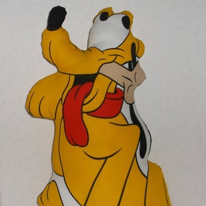 May include: A yellow and white plush toy of Goofy, a cartoon dog character from Disney. Goofy is wearing a red scarf and has a black nose and eyes.