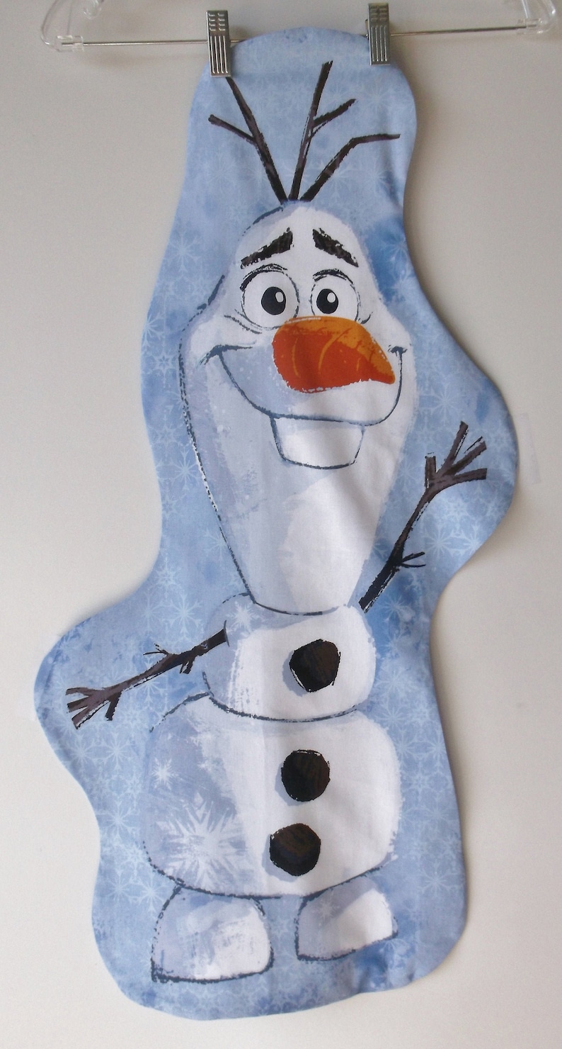 May include: A blue fabric stocking with a white snowman design. The snowman has a carrot nose, black eyes, and a black mouth. The snowman is wearing a white hat with a brown brim. The stocking is decorated with a snowflake pattern.