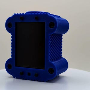 Puede incluir: Un objeto rectangular azul impreso en 3D con un panel frontal negro liso. El marco azul presenta un patr&oacute;n lateral texturizado y acanalado, con cuatro fijaciones circulares negras en las esquinas y detalles negros adicionales en los bordes.