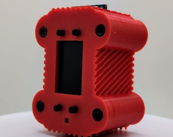 Puede incluir: Una carcasa electrónica rectangular de color rojo brillante impresa en 3D con una pantalla negra central. El exterior presenta una superficie texturizada y acanalada, cuatro orificios circulares para tornillos en las esquinas y cuatro botones negros.