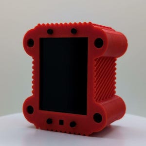 Puede incluir: Un marco rectangular rojo impreso en 3D con una superficie texturizada y estriada y un panel central negro liso. El marco presenta cuatro recortes circulares en las esquinas y peque&ntilde;os detalles circulares negros en los bordes superior e inferior.
