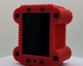 May include: A rectangular red 3D-printed frame with a textured, ridged surface and a smooth black center panel. The frame features four circular corner cutouts and small black circular accents along the top and bottom edges of the structure.