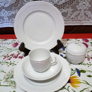 May include: White porcelain tea set with a delicate embossed design. The set includes a cup, saucer, plate, and sugar bowl.