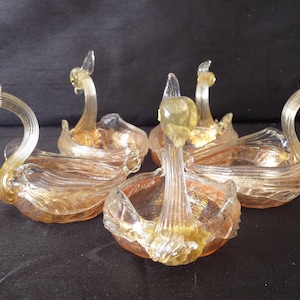 May include: Set of five clear glass swan-shaped dishes with gold accents. The dishes are arranged in a circle, with the necks of the swans pointing outwards.
