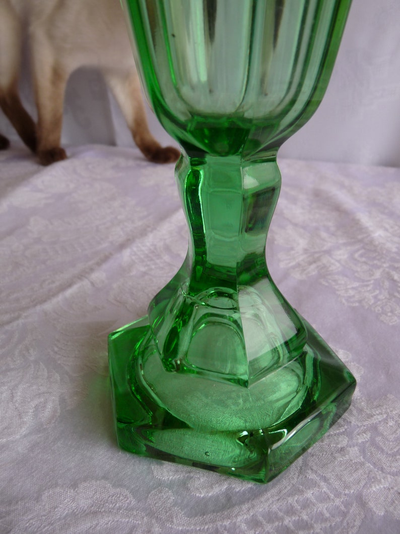 May include: A green glass goblet with a faceted base. The goblet is made of clear glass with a green tint.