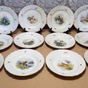May include: Set of 12 white porcelain dinner plates with gold trim and hand-painted scenes of birds and animals in a woodland setting.