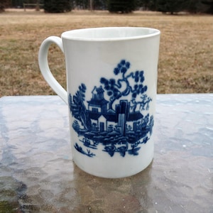 Op de afbeelding: Een witte keramische mok met een blauw en wit ontwerp van een Chinees landschap. De mok heeft een handvat en is versierd met een traditioneel Chinees patroon.